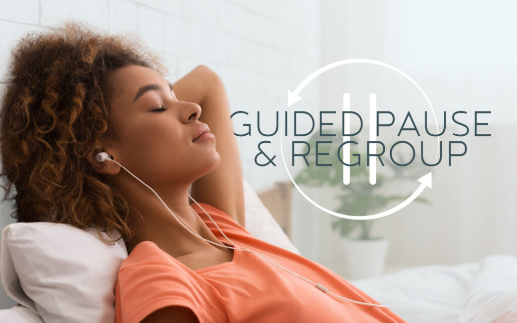 A Black woman in an orange shirt is relaxing on a couch, leaning into pillows with her eyes closed.  She has earbuds in and is listening to the Guided Pause & Regroup by Michelle Puster of Compassionate Heart Mindful Life.  