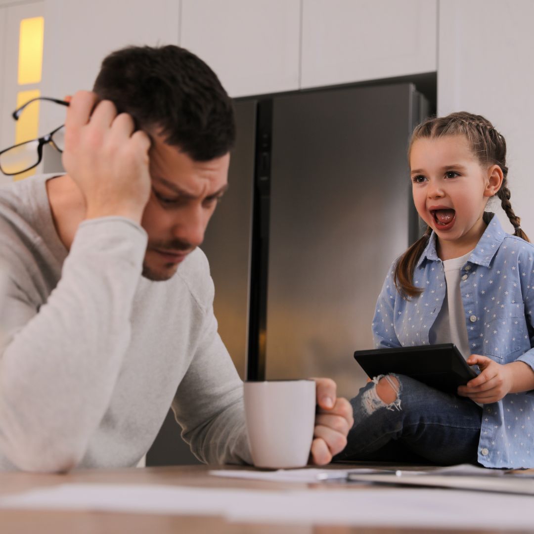 Father concentrating on paperwork while young daughter with tablet yells nearby.